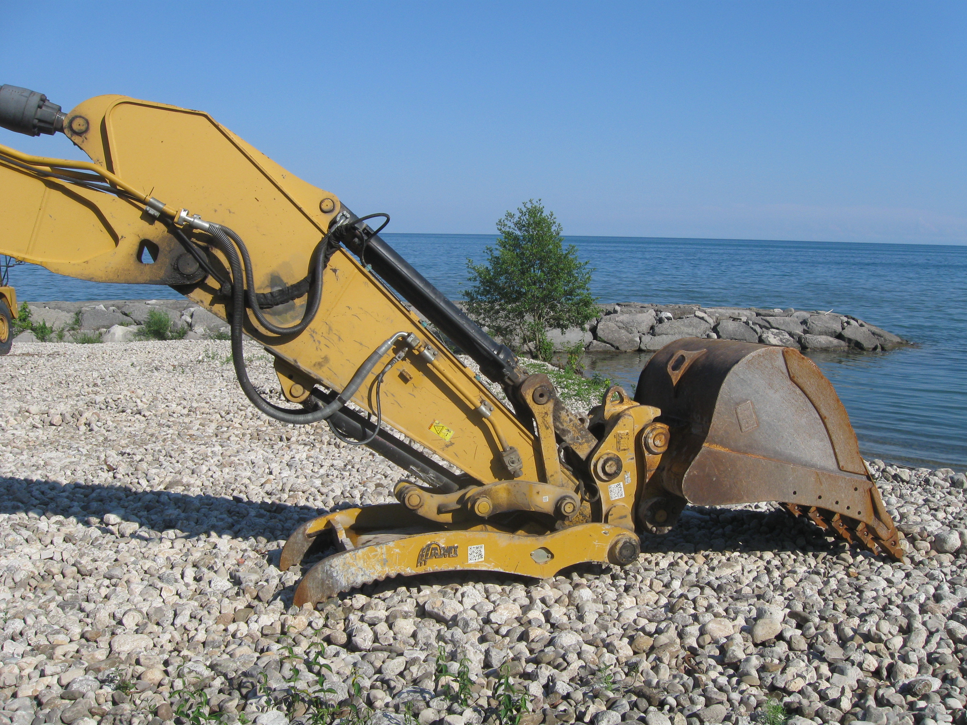 an excavators tool-end resting open on the stoney shore of rouge hill